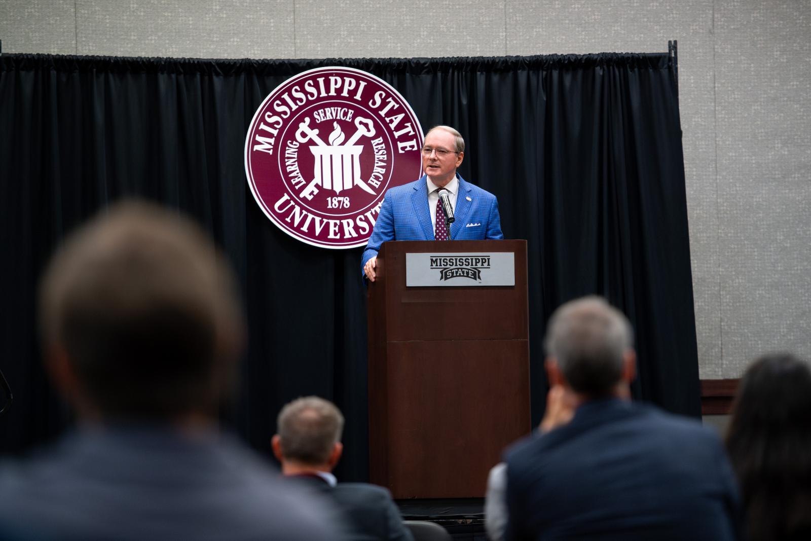 man in blue blazer speaks at podium