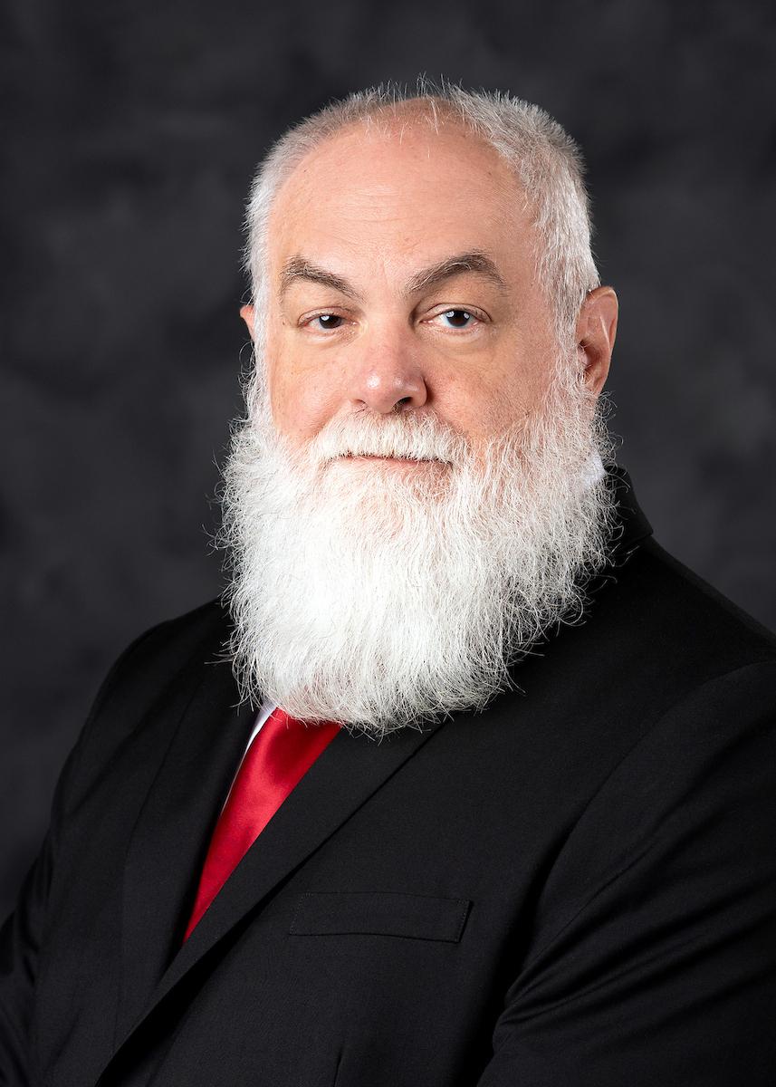 Headshot of Michael Cox on a dark background in black suit and red tie