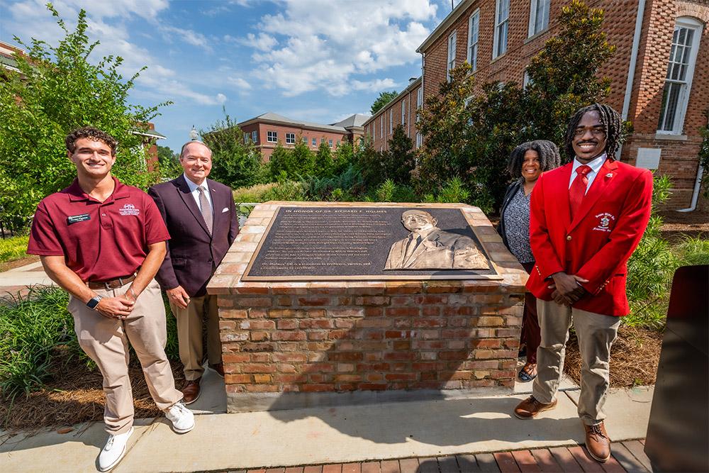 Two student leaders stand with the university president and a vice president by a newly dedicated monument in honor of Dr. Richard E. Holmes