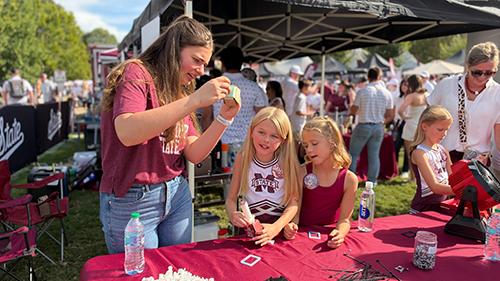 Mississippi State IDEELab student Anna Box helps students at the final building and quality station of the cowbell-making process during pregame festivities at the Junction on Sept. 26.