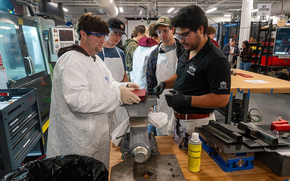 Mississippi State IDEELab instructor Alejandro Martinez guides ACE Composites participants through a hands-on tooling and finishing exercise, demonstrating proper material handling, trimming, clamping and post-processing techniques used in composite manufacturing.