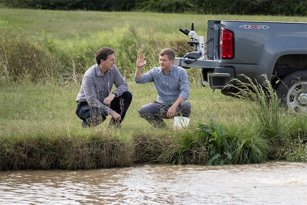 Dr. Mark Lawrence, left, and Dr. Stephen Reichley look at a water sample while kneeling by a fish pond